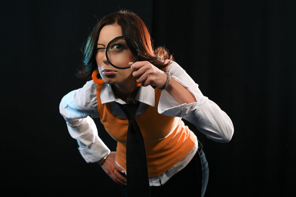 Young woman holding magnifying glass like detective.