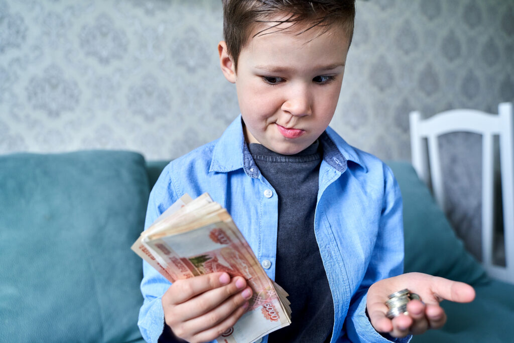 A child with paper money in one hand and small coins in the other hand