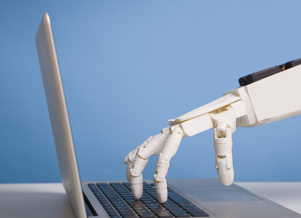 Internet bots concept. Robotic hand typing on laptop keyboard.